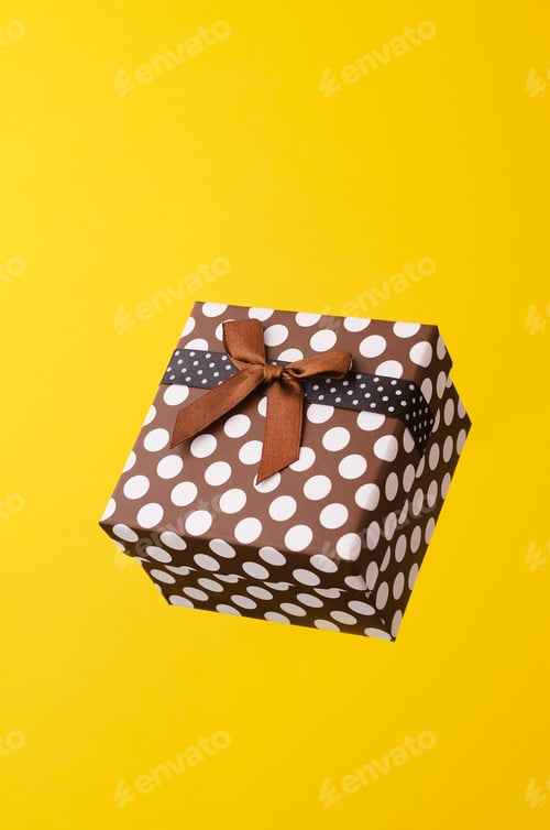 Preview: Gift Box With Dots Floating In The Air Over Bright Yellow Background