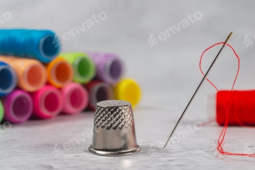 Preview: Close-Up View Of One Needle With Red Thread And Thimble With Differently Colored Spools Of Thread