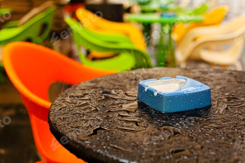 Preview: Wet Table With Blue Ashtray And Empty Seats Of Coffee Shop In The Background