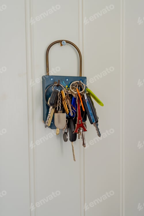 Preview: Several Keys And Keychains Hanging On Hooks On A White Wall.