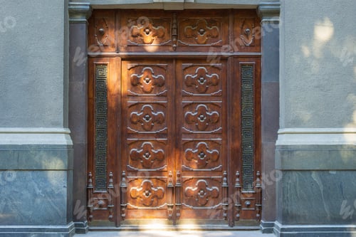 Preview: Carved Wooden Double Closed Door Illuminated By Sunspots On A City Street