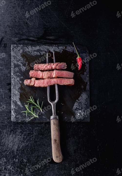 Preview: Grilled Striploin Angus Steak Cut In Pieces On The Fork On Sate Stone Board. Top View. Copy Space