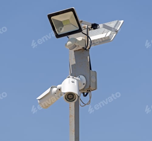 Preview: Surveillance Cctv Cameras And Led Floodlight Mounted On Post Against The Blue Sky