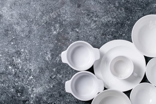Preview: Variety Of Empty White Ceramic Plates And Bowls Over Dark Texture Background. Top View, Flat Lay