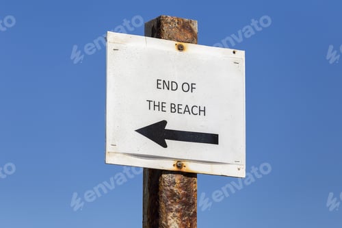 Visualização: Placa de metal no final da praia com fundo de céu azul.