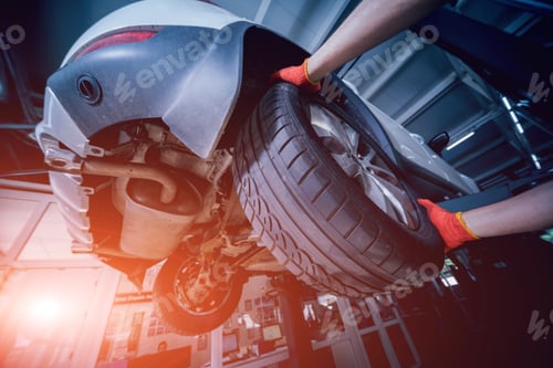 Preview: Car Mechanic Inspecting Wheel And Suspension Detail Of Lifted Automobile At Repair Service Station