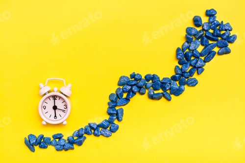 Preview: White Alarm Clock And A Road Made Of Decorative Stones On A Yellow Background. Leaking Time Concept