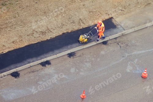 Preview: A Worker Lays Asphalt With A Hand Roller On The Sidewalk Near The Road
