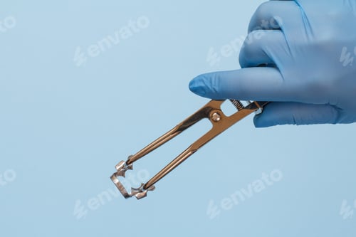 Preview: Dentist'S Hand In A Latex Glove With Dental Tongs And Clasp On Blue Background. Medical Tools