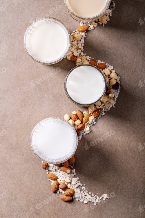 Preview: Almond, Hazelnut, Oat And Rice Milk Served With Nuts Over Brown Texture Background. Top View, Flat