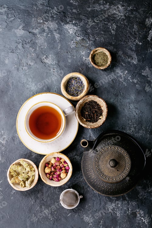 Preview: Black And Green Tea In A Ceramic Cups With Black Metal Teapot And Rose Petals Over A Dark Texture