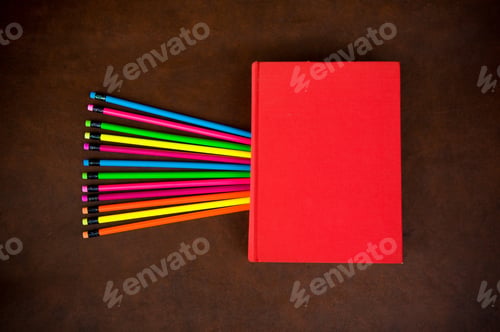 Preview: Wooden Desktop With Colorful Pencil And Red Book With Empty Cover