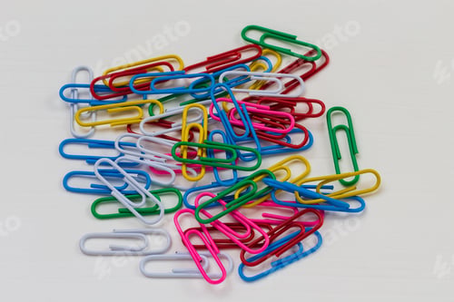 Preview: Many Multi-Colored Paper Clips Lie On A White Wooden Table. Background