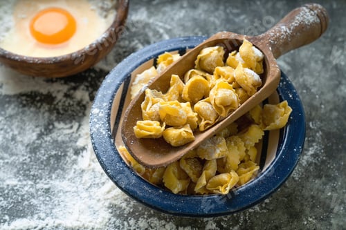 Preview: Raw Uncooked Cappelletti In A Vintage Olive Tree Scoop A Blue Ceramic Bowl Over Metal Background