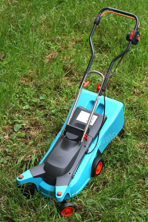 Preview: Electric Lawn Mower Stands On Green Unmown Grass In Cloudy Weather