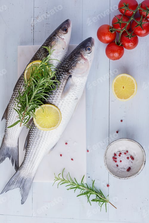 Preview: Fresh Mullet On A Marble Board Over Vintage Wooden Background With Rosemary, Lemon And Tomatoes