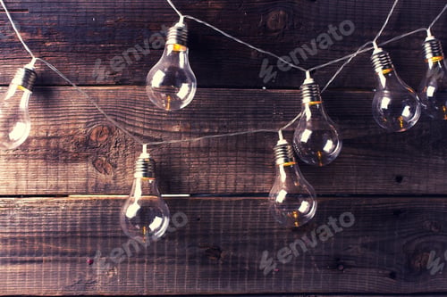 Preview: Burning Garland From Light Bulbs On Rustic Weathered Wooden Background. Selective Focus. Place For