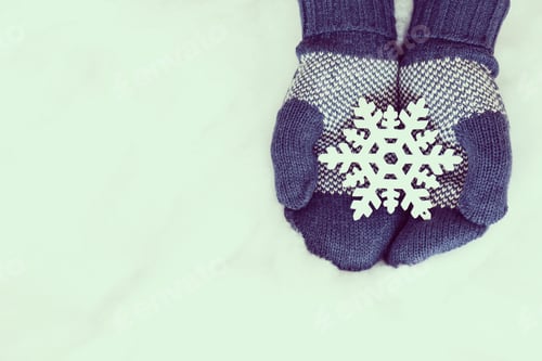 Preview: Woman Hands In Light Teal Knitted Mittens Are Holding Snowflake On Snow Background. Winter And