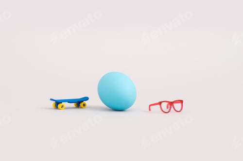 Preview: Creative Concept With Blue Egg, Eyeglasses And Skateboard On Grey Background