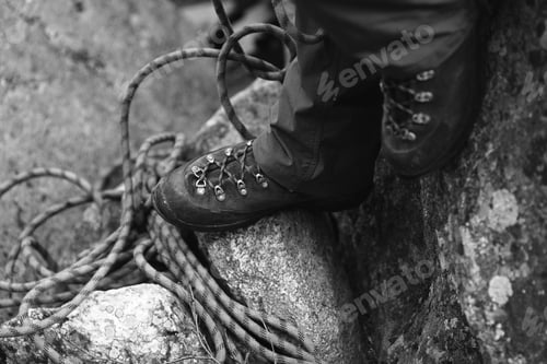 Preview: Legs Of The Climber In Climbing Boots Against The Backdrop Of Climbing Rope. Black And White.