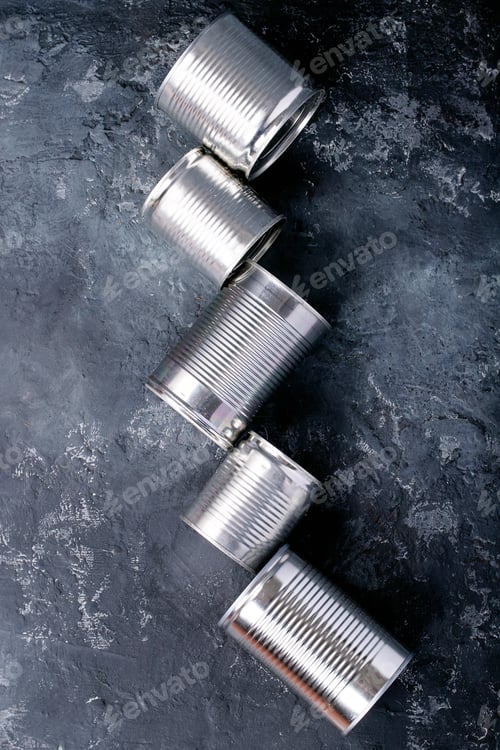 Preview: Canned Food In Metal Cans Over Dark Texture Background. Copy Space. Food Supply Concept. Top View