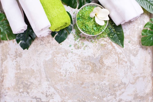 Preview: Organic Skin Care Flat Lay. Bowl With Green Sea Salt, White Towels, Tropical Leaves On Grey
