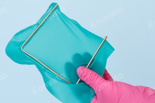 Preview: Dentist'S Hand In A Pink Latex Glove With Dental Cofferdam Scarf And Frame On Blue Background