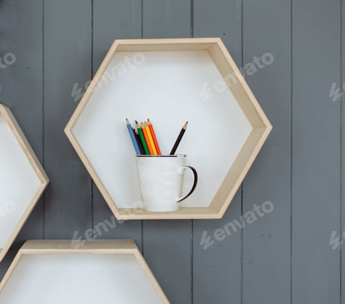 Preview: Hexagonal Bookshelf On Grey Wall. Glass With Colored Pencils On The Shelf. Empty Hexagons Wooden