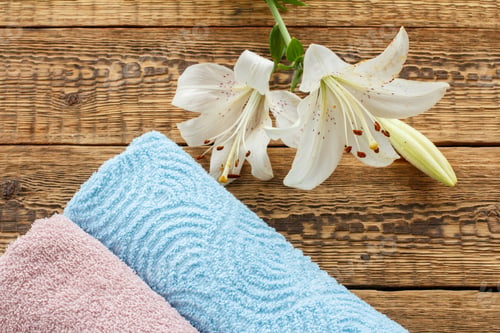 Preview: Blue And Pink Soft Terry Towels With White Lily Flowers On Old Wooden Boards. Top View.