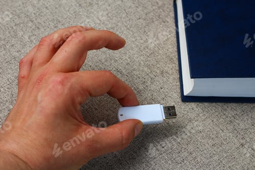 Preview: A Flash Drive In Hand On A Background Of A Book. Knowledge Loading Metaphor