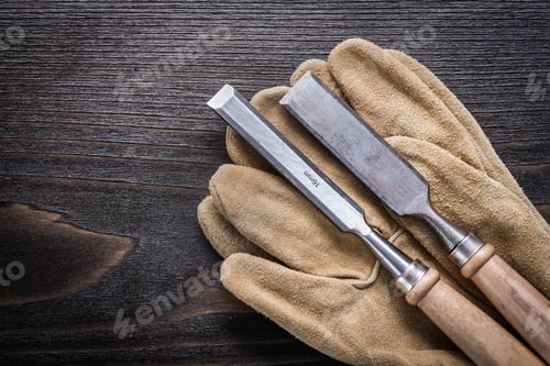 Preview: Pair Of Leather Working Gloves With Flat Chisels On Vintage Wooden Board Construction Concept.
