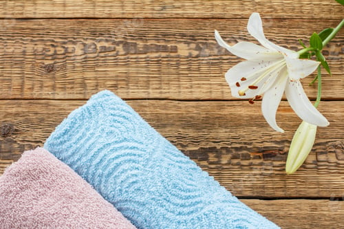 Preview: Blue And Pink Soft Terry Towels With White Lily Flower On Old Wooden Boards. Top View With Copy