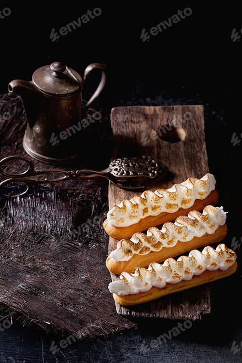 Preview: Home Made Eclairs Decorated With White Meringue On The Rustic Wooden Serving Board With A Metal