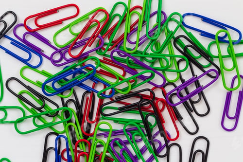 Preview: Many Multi-Colored Paper Clips Lie On A White Wooden Table. Background