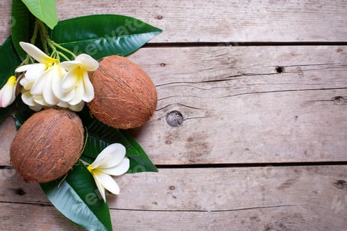 Preview: Two Coconuts On Leaves And Plumeria Flowers On Aged Wooden Background. Selective Focus. Flat Lay