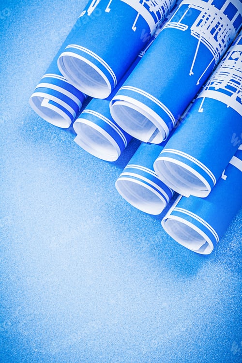 Preview: Pile Of Rolled Blueprints On Blue Background Vertical View.