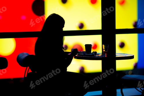 Preview: Silhouette Of Woman Eating Breakfast At The Bar. Colorful Background Opposed To The Model.