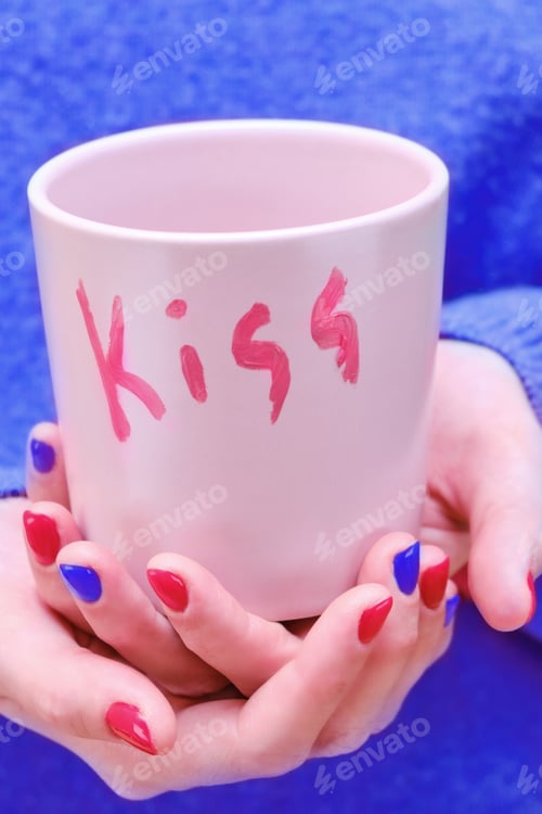 Preview: A Woman In A Blue Sweater Holds A Pink Cup With The Words Kiss