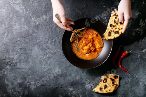 Preview: Chicken Tikka Masala Spicy Curry Meat Served In Black Ceramic Plate With Female Hands Over Wooden