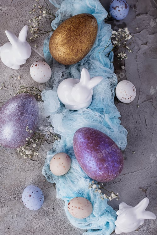 Preview: Chocolate Easter Eggs Decorated With Ceramic Bunnies And Blue Napkin Over A Gray Stone Background
