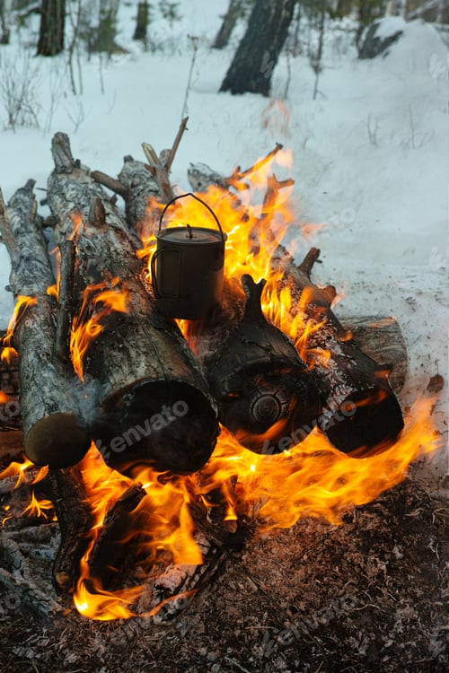 Preview: A Tourist Titanium Mug For Boiling Water Stands On Firewood In A Burning Bonfire In The Winter