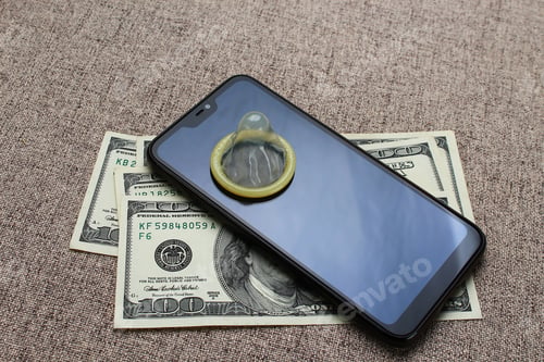 Preview: Unpacked Condom, Telephone And A Lot Of Denominations Of 100 Dollars On A Background Of A Sofa