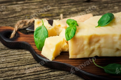 Preview: A Piece Of Parmesan Cheese With Basil Leaves And Cheese Knife On A Wooden Board