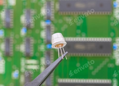 Preview: Electronic Component Held With Tweezers Over A Green Motherboard