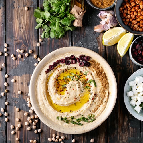 Vista previa: Hummus With Olive Oil And Ground Cumin In Ceramic Bowl Served With Lemons, Olives, Feta Cheese