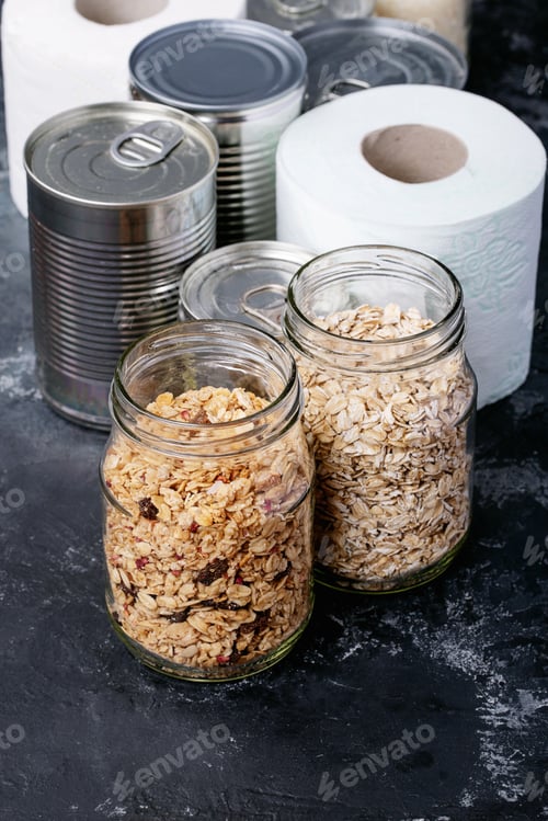 Preview: Canned Food In Metal Cans With Oats, Rice In Glass Jars Over Dark Texture Background. Copy Space