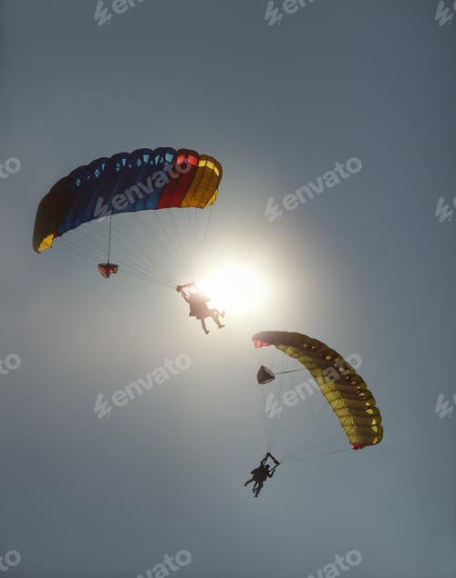 Preview: Two Tandem Parachute Canopy With Skydiver Silhouettes Against The Sky And A Dazzling Sun Disk.