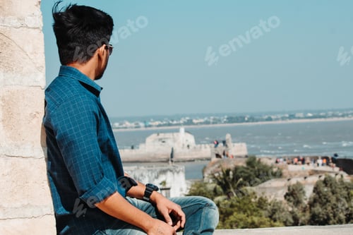 Preview: Young Indian Man Sitting On A Wall And Looking At The Arabian Sea At Diu Fort In Diu, India