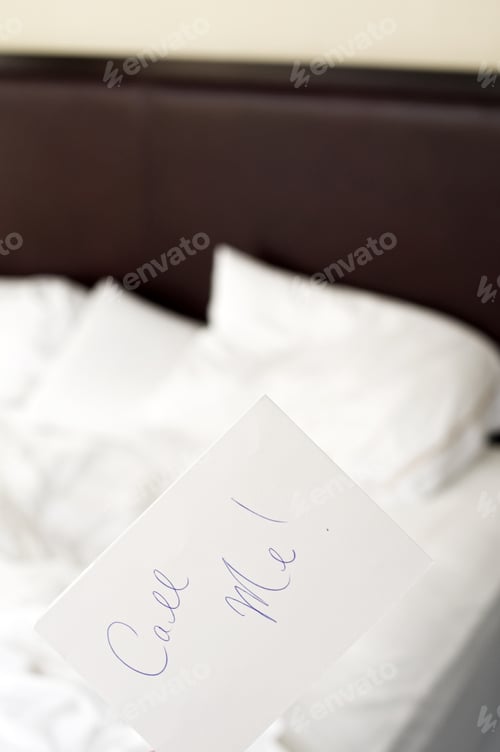 Preview: Selective Focus Of A Note Held Above A Bed With Rumpled White Sheets And Pillows.