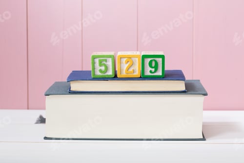 Preview: 529 College Savings Plan Concept With Textbooks Stacked In Front Of A Pink Wooden Background With